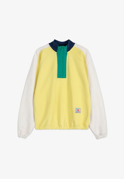 Pullover giallo con maniche bianche, colletto blu e mezza zip verde. Presenta un orlo elastico e una toppa con logo in basso a sinistra.