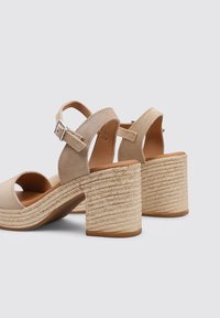 Tacones de ante beige, destalonados, con un tacón grueso de cuerda trenzada. Correa ajustable en el tobillo con hebilla plateada. Plantilla de cuero suave.