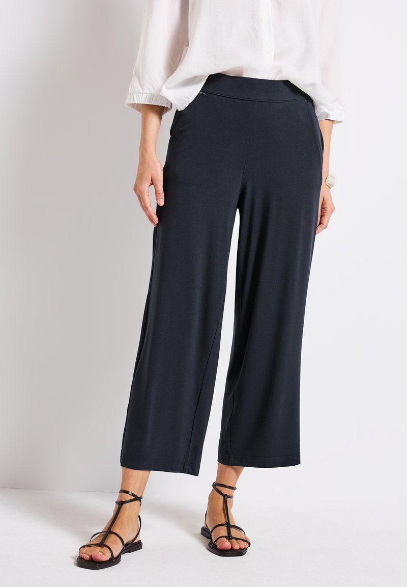 Dark navy wide-leg pants with an elastic waistband, crafted from soft fabric, paired with strappy black sandals.