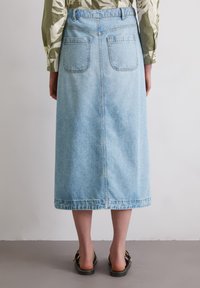 Light blue denim midi skirt with two back pockets, a straight cut, and a raw hem. Accompanied by black flat sandals.