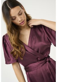 Burgundy wrap dress in textured fabric, featuring short sleeves, a deep V-neckline, and a self-tie belt at the waist.