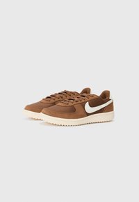 Bruine sneakers van suede en mesh, met een wit Nike-logo, ronde neus en een gestructureerde rubberen zool, en platte veters voor een stevige pasvorm.