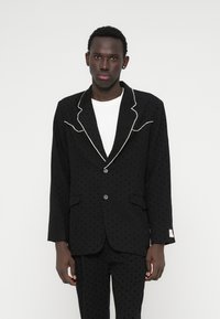 Czarna marynarka z teksturą w groszki, kontrastowym białym wykończeniem na klapach oraz dwoma guzikami. Posiada boczne kieszenie oraz dopasowany krój.