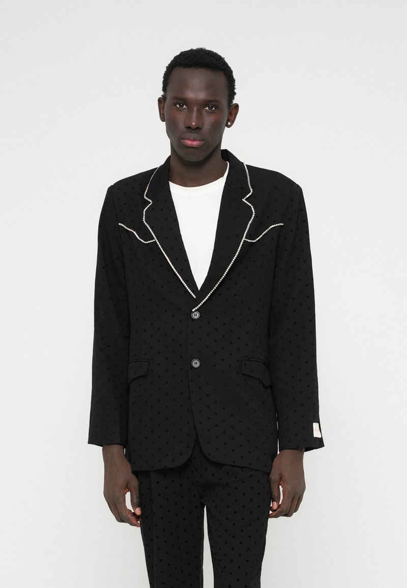 Czarna marynarka z teksturą w groszki, kontrastowym białym wykończeniem na klapach oraz dwoma guzikami. Posiada boczne kieszenie oraz dopasowany krój.