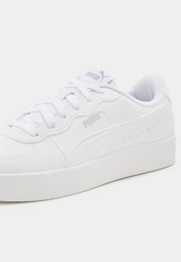 Baskets en cuir blanc avec semelle plate, bout rond et accents texturés. Présentent un logo sur le côté et le dessus, complétés par des lacets blancs.