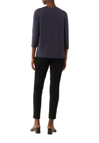 Marineblaues Top mit drei Viertelärmeln aus glattem Stoff, kombiniert mit schwarzen Slim-Fit-Hosen und schwarzen High-Heels. Einfaches, klares Design.