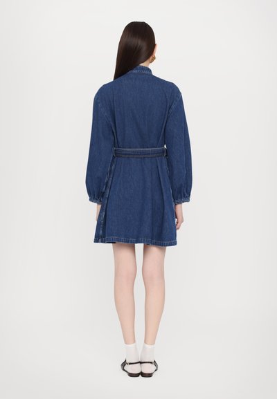Rochie din denim cu mâneci lungi și talie cu curea, având un guler clasic și fustă evazată, într-o nuanță bleu medie cu un material texturat.