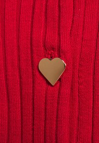 Pendentif en forme de cœur en or sur un tissu tricoté rouge avec un motif de côtes verticales.
