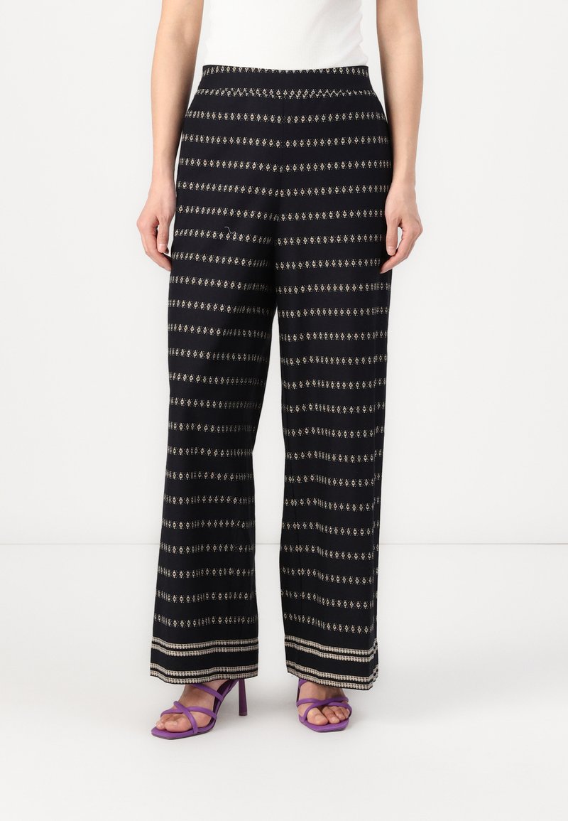 Μαύρα παντελόνια με φαρδιά μπατζάκια και χρυσά γεωμετρικά σχέδια, με επίπεδη μέση και στρίφωμα που τονίζεται από μια ελαφριά αντίθεση.