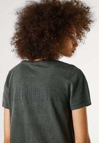 Hallhalli hallhalli t-särk, lühikeste varrukatega, ümmarguse kaelusega ja sõnaga "LONDON" narmastega detailiga seljal. Sile tekstuur, mugav lõige.