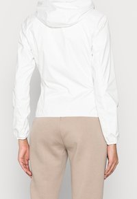 Hvid letvægtsjakke med hætte, elastiske manchetter og tætsiddende design. Glat tekstur og minimalistisk stil.