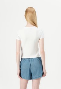 Camiseta blanca de manga corta acompañada de pantalones cortos de estilo denim azules con cintura elástica. Diseño simple y limpio con un ajuste relajado.