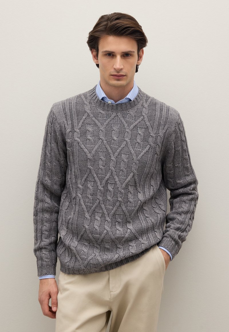 Grauer Strickpullover mit Rundhalsausschnitt und strukturiertem Rautenmuster, getragen über einem hellblauen Hemd mit Kragen und beiger Hose.