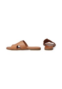 Læder slip-on sandaler i tan, med et krydsrem-design og åben tå. Flad sål med minimal tekstur og buede kanter.
