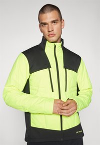 Giacca zip-up giallo brillante e nera con texture trapuntata, colletto alto, due tasche con cerniera e sezioni di colore in contrasto.