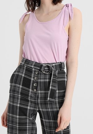 Růžový tílkový top s mašličkovými ramínky v kombinaci s černobílými kostkovanými kalhotami s vysokým pasem, bočními knoflíky a páskem.