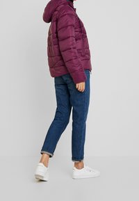 Fioletowa puchowa kurtka z kapturem, z poziomym pikowaniem i ściągaczem w talii. W zestawie z dżinsami z podwiniętymi nogawkami i białymi trampkami.