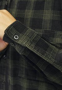 Zwart en groen geruite corduroy overhemd, met een knoopmanchet en textuurstof, met zichtbare stiksels en geruite patroon details.