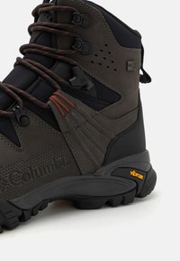 Ciemnoszare buty trekkingowe z teksturowanym zamszem i siateczką, kontrastującymi czerwonymi sznurowadłami oraz podeszwą Vibram zapewniającą przyczepność. Posiadają wodoodporną konstrukcję.