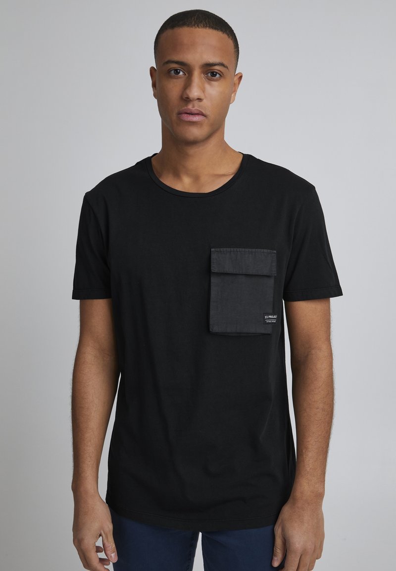 T-shirt en coton noir avec un col rond, des manches courtes et une poche plaquée texturée sur la poitrine gauche. Design simple, sans motifs.
