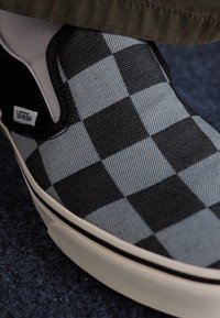 Zapatillas Vans slip-on con un patrón de tablero de ajedrez en blanco y negro, tela texturizada, suela de goma blanca y acentos en negro.