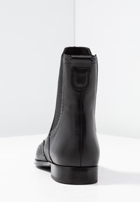 Musta nahkainen nilkkurit, joissa on sileä pinta, pyöreä kärki, näkyvät saumat, vedin takaosassa ja matala, mattapintainen korko.