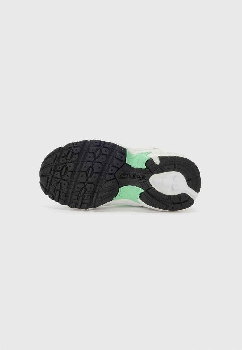 Semelle extérieure en caoutchouc noir avec des accents verts, présentant des motifs de semelle texturés pour une meilleure adhérence et une semelle intermédiaire blanche au fini lisse.