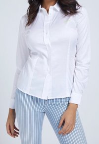 Chemise blanche à boutons, à manches longues, au design ajusté et avec un détail de logo subtil. Associée à un pantalon rayé bleu et blanc.