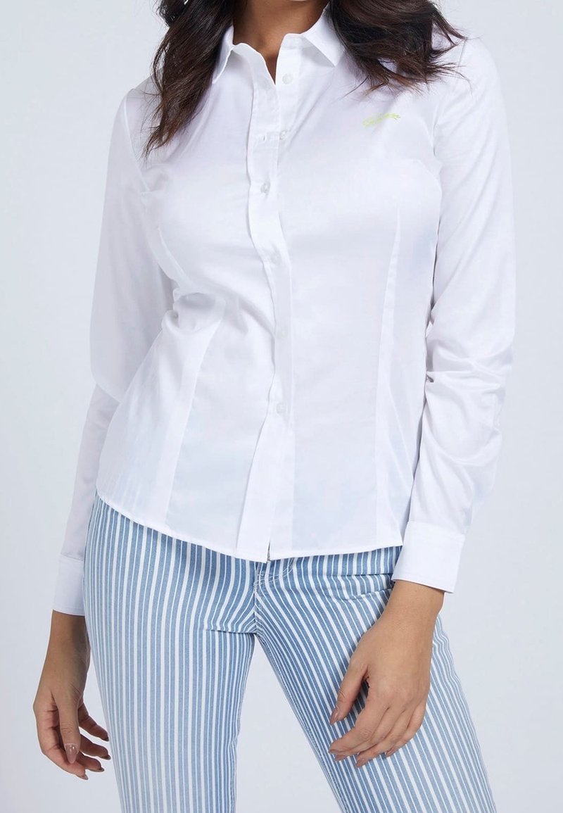 Chemise blanche à boutons, à manches longues, au design ajusté et avec un détail de logo subtil. Associée à un pantalon rayé bleu et blanc.