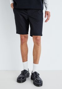 Svarta shorts i lätt tyg, med rak passform. Kommer med svarta skor, vita strumpor och en mörk skjorta.