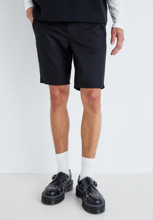 Black shorts made of lightweight fabric, featuring a straight cut. Paired with black shoes, white socks, and a dark shirt.