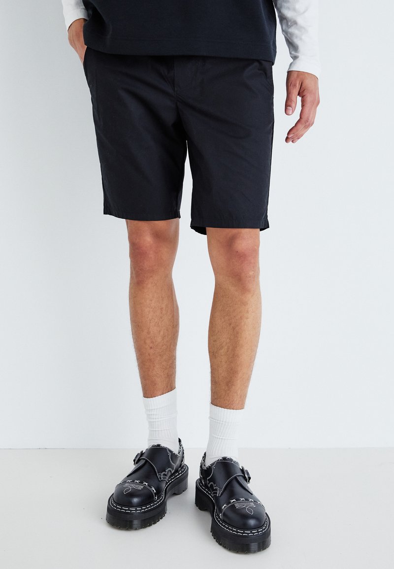 Svarta shorts i lätt tyg, med rak passform. Kommer med svarta skor, vita strumpor och en mörk skjorta.