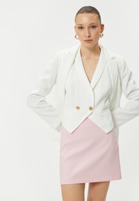Blazer blanc avec des boutons dorés doubles, associé à une mini-jupe rose ajustée. Tissu lisse avec une coupe nette et un design structuré.