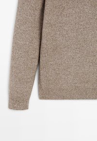 Un maglione beige lavorato a maglia presenta un tessuto morbido e testurizzato con polsini e orlo a coste. Il design è semplice e morbido, con maniche lunghe.