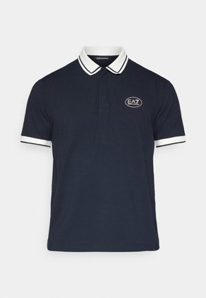 Tmavě modré polo tričko s bílým lemovaným límečkem, krátkými rukávy a logem vyšitým v oválu na levé hrudi.