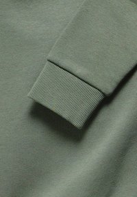 Primo piano di un tessuto di felpa verde; presenta polsini a coste, una texture morbida e una superficie liscia. Colorazione uniforme su tutto il materiale.