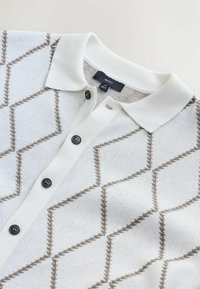 Weißes Strick-Polohemd mit braunem geometrischem Muster, drei schwarzen Knöpfen am Kragen und einer weichen Textur. Markenlabel ist innen sichtbar.