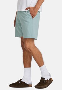 Light blue shorts with a smooth texture, side pockets, and a relaxed fit, paired with white socks and brown slip-on shoes.