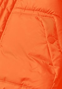 Tessuto di una giacca a vento arancione brillante con una tasca visibile e dettagli di bottone. La superficie è liscia con una texture trapuntata.