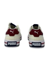 Sneaker Puma con una toma beige, un accento in pelle rossa sul tallone e una suola bianca e blu texturizzata con un logo prominente sul retro.
