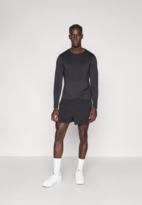 Fekete hosszú ujjú felső és rövidnadrág szett, testhezálló szabásban. A szövet sima textúrájú, minimalista stílusú, fehér tornacipővel és zoknival párosítva.