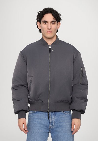 Veste bomber grise avec fermeture éclair à l'avant, poignets côtelés et poche latérale. Fabriquée en matériau lisse et léger avec une coupe décontractée.