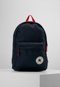 Námořnický látkový batoh s červenými akcenty. Obsahuje přední kapesní zip a kulatou nášivku s logem. Zaoblený tvar s nastavitelnými popruhy.