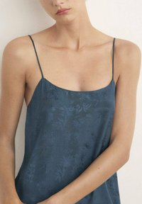 Camisola blu scuro con motivo floreale, dotata di sottili spalline a spaghetti e una consistenza morbida e liscia. Presenta una silhouette rilassata e fluida.
