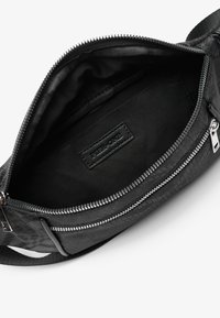 Black crossbody bag with a textured exterior, featuring a smooth zipper closure, lined interior, and a logo patch on the inside.