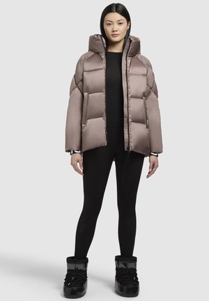Giacca puffer marrone chiaro con cappuccio, con un design trapuntato, zip frontale e polsini elasticizzati. Indossata sopra un top nero e leggings.
