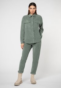 Grünes Cordhemd und Hosen-Set, bestehend aus einem Hemd mit Kragen und Knopfschluss, zwei Brusttaschen und knöchellangen Hosen.