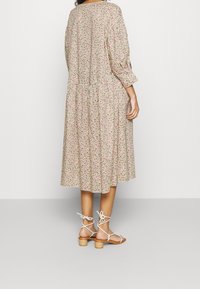 Vestido midi floral con cintura fruncida, mangas de ¾ de longitud y fondo beige. Presenta patrones en rosa y verde. Combinado con sandalias con tiras.