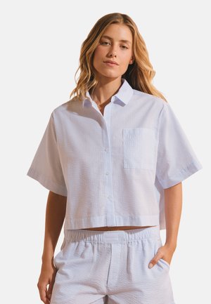 Donna con capelli biondi lunghi che indossa una camicia di seersucker azzurra a maniche corte con tasca frontale e pantaloncini abbinati con vita elastica.