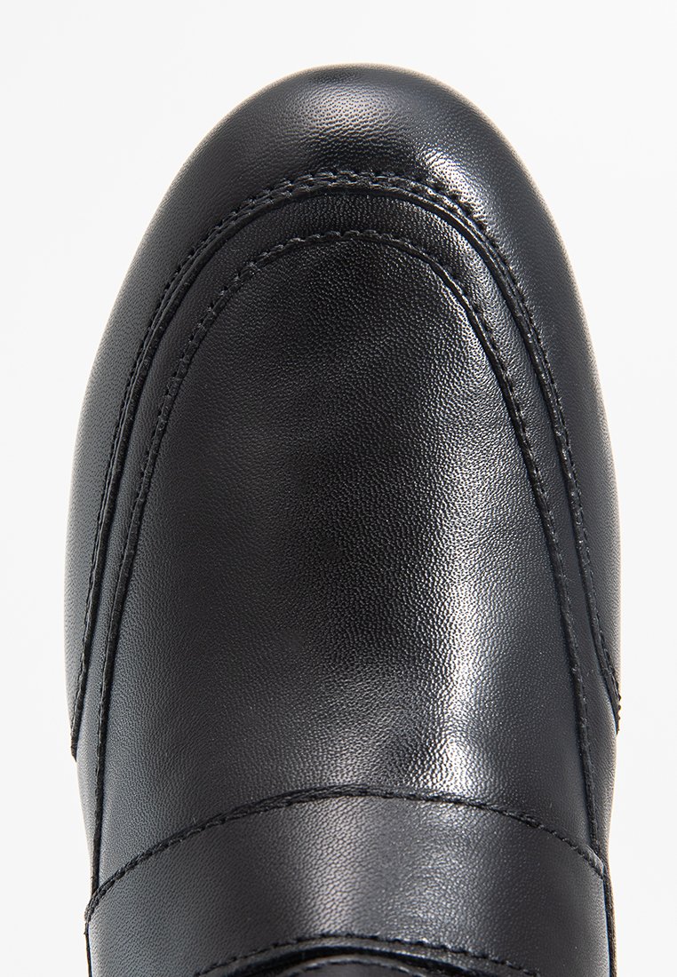 Chaussure en cuir noir avec une finition lisse, bout arrondi et des détails cousus sur les côtés. Présente un profil bas et un design minimaliste.